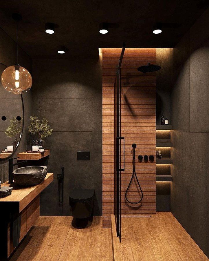 A bathroom with a large tub in the middle of it and wooden flooring next to a wooden table in front of a bathroom with black bench, brass accent lighting, brass finishes, dark painted door, antique rug. Foyer Design,